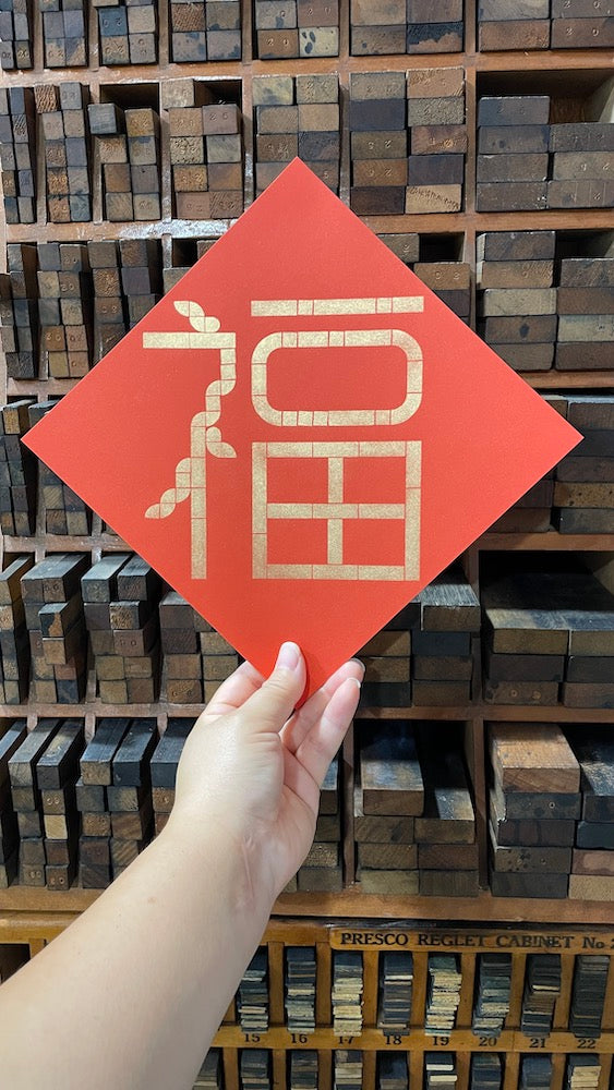 A hand is holding the diamond shaped red paper with "Foo" printed in gold