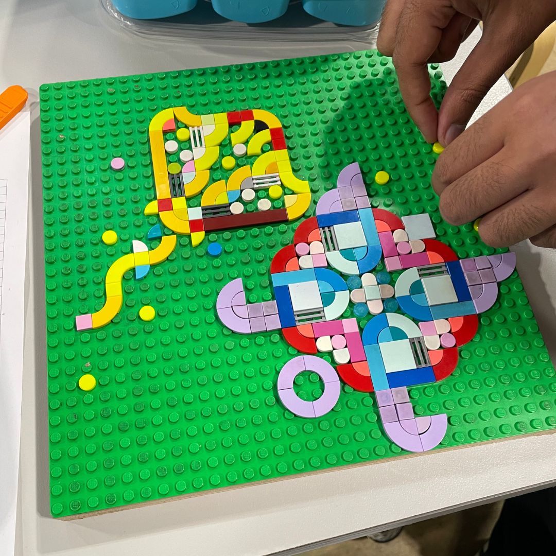 Close up of a pair of hands working on a lego letterpress design featuring a sea turtle and a manta ray on a lego base plate.