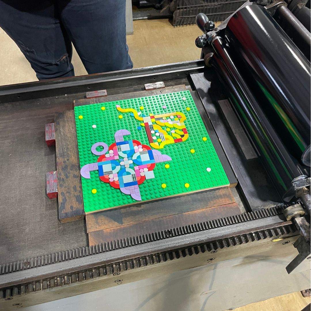 On the Vandercook press ready to be printed is a lego base place with a lego tile design featuring a sea turtle and a manta ray.