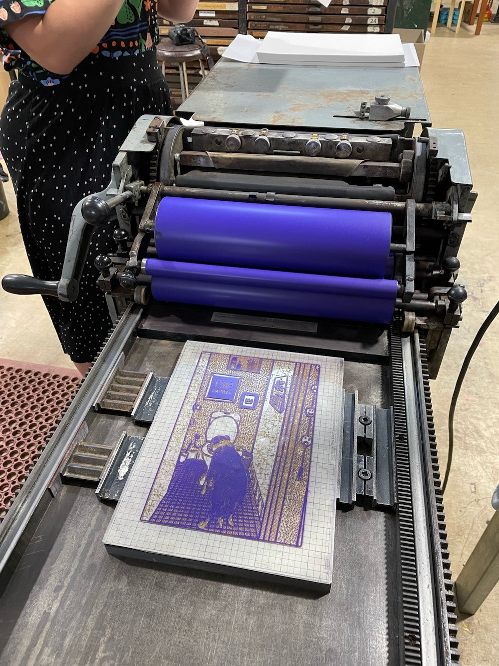 Work in progress featuring the printing plate on the vandercook press and the press has a vibrant purple ink on the rollers.